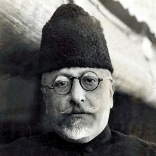 Close black-and-white portrait of Maulana Abul Kalam Azad wearing round spectacles and a tall karakul cap.