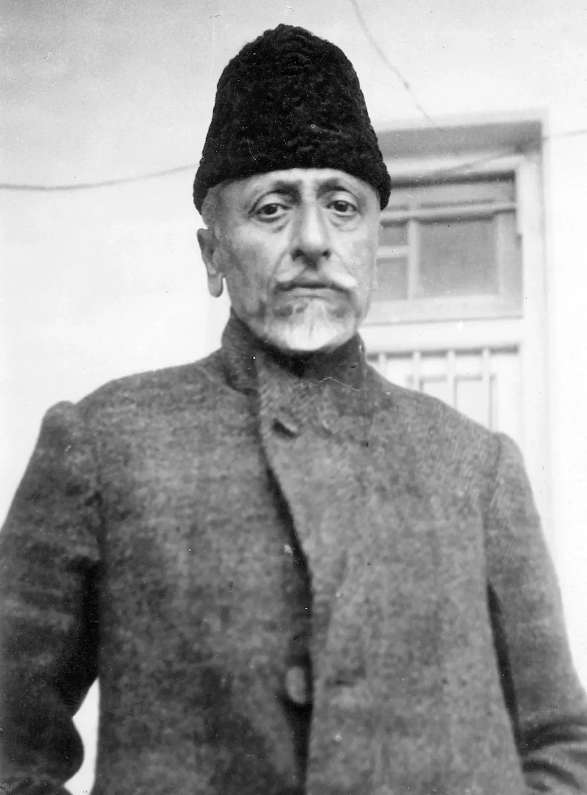 Full-length black-and-white photograph of Maulana Abul Kalam Azad standing outdoors in a heavy coat and karakul cap.